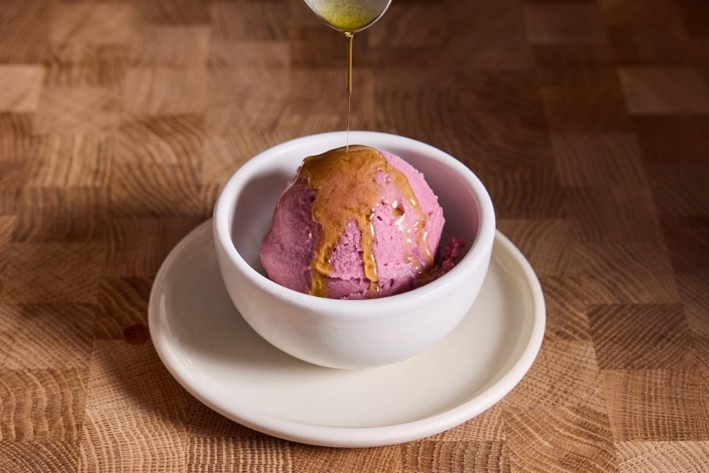 olive pil is drizzled atop a white cup and saucer filled with purple sorbet 