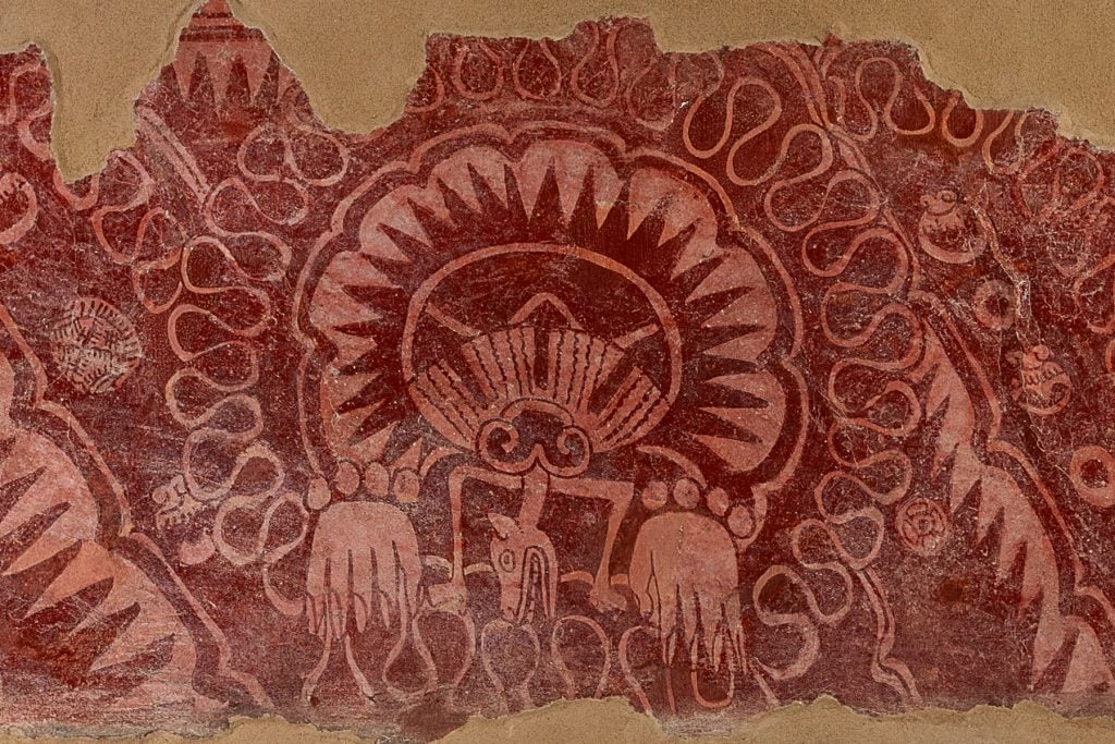 red mural painting of ancient mesoamerican symbols that includes various animals gathering around a central object