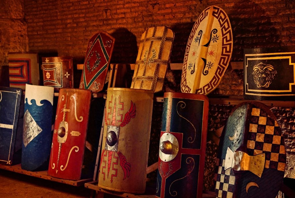 A row of decorated shields is laid out in the Colosseum experience. 