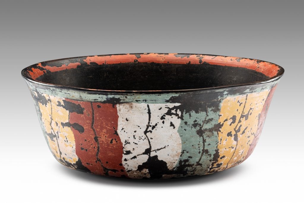 a small ceramic bowl from long ago showing cracks breaking through faded coats of yellow red white and green paint