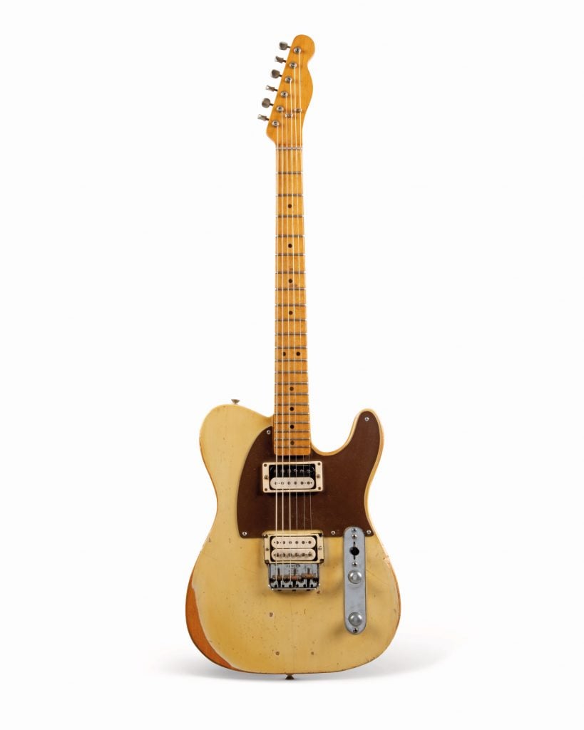 a light wood colored guitar standing upright on a white background