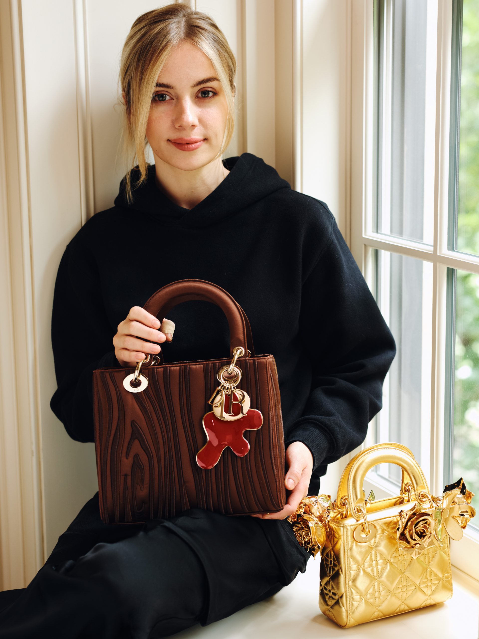 a blonde woman Vlad in black sits in a windowsill and has two colorful purses