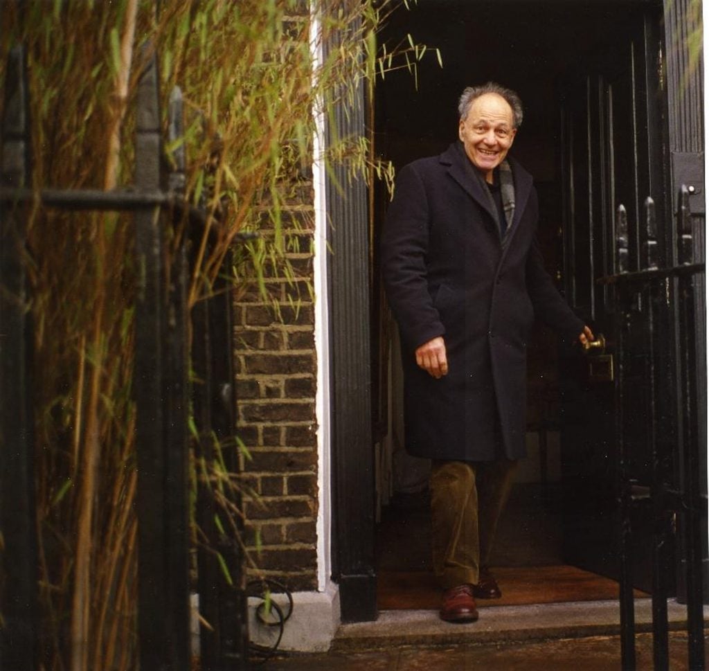 a man in a dark coat steps out of a front door of a brick house