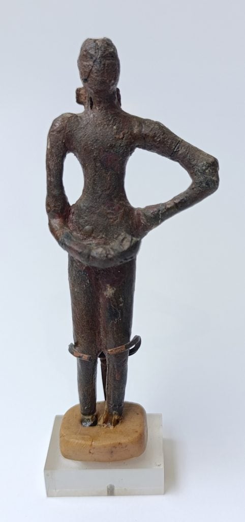 A bronze sculpture of a woman standing upright with her left hand on her hip