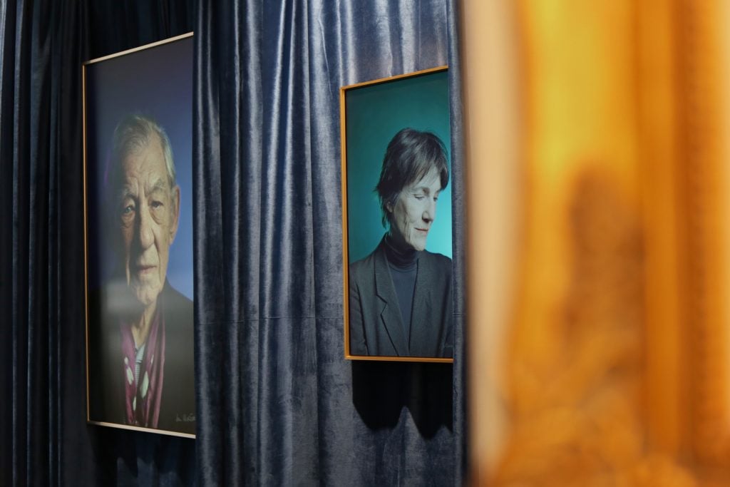 two portraits are seen against a gray curtain