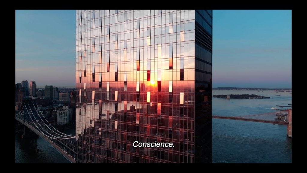 Carissa Rodriguez, Conscience. A film still of a glass Brooklyn skyscraper with the sunset reflected on the facade, with the East River and Lower Manhattan behind it. 