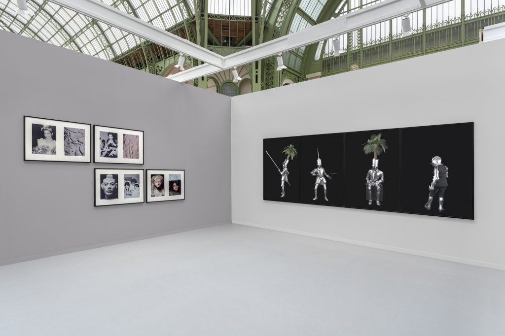 An exhibition space features black-and-white framed photographs on one wall and a series of digital artworks showing armored figures with plants on their heads on another. The setting is within a bright, glass-roofed hall.