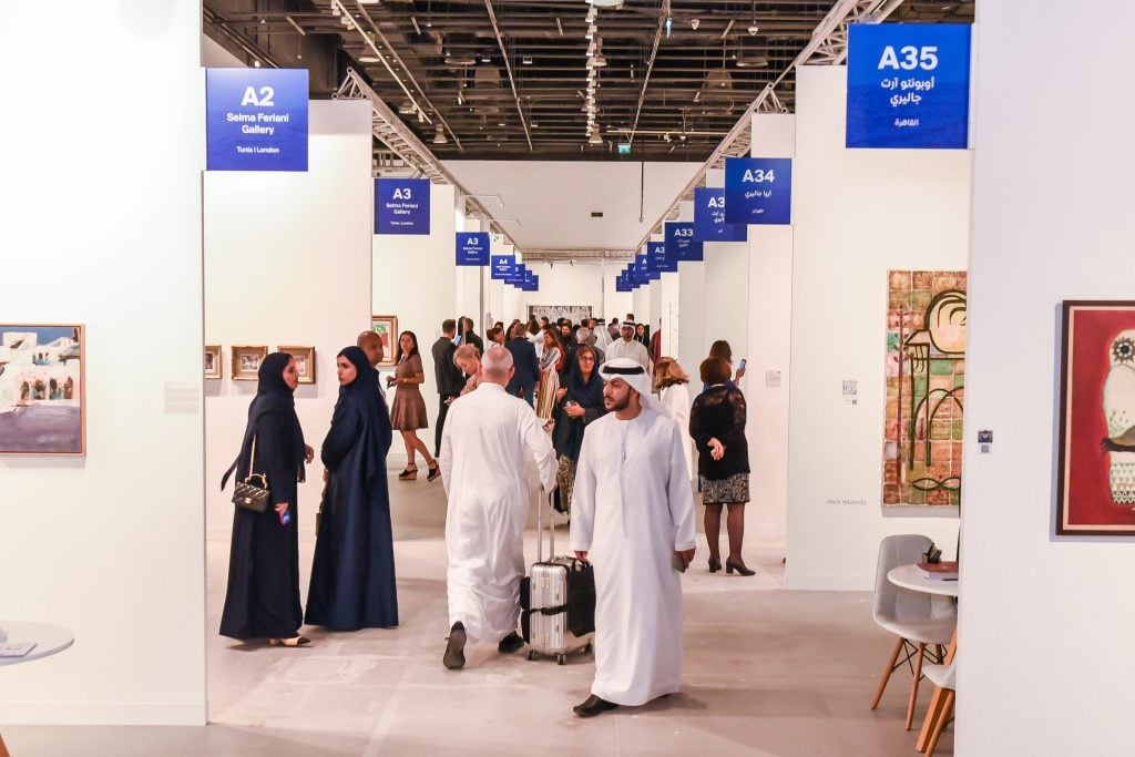 Visitors explore a contemporary art fair with gallery booths displaying paintings and artworks.