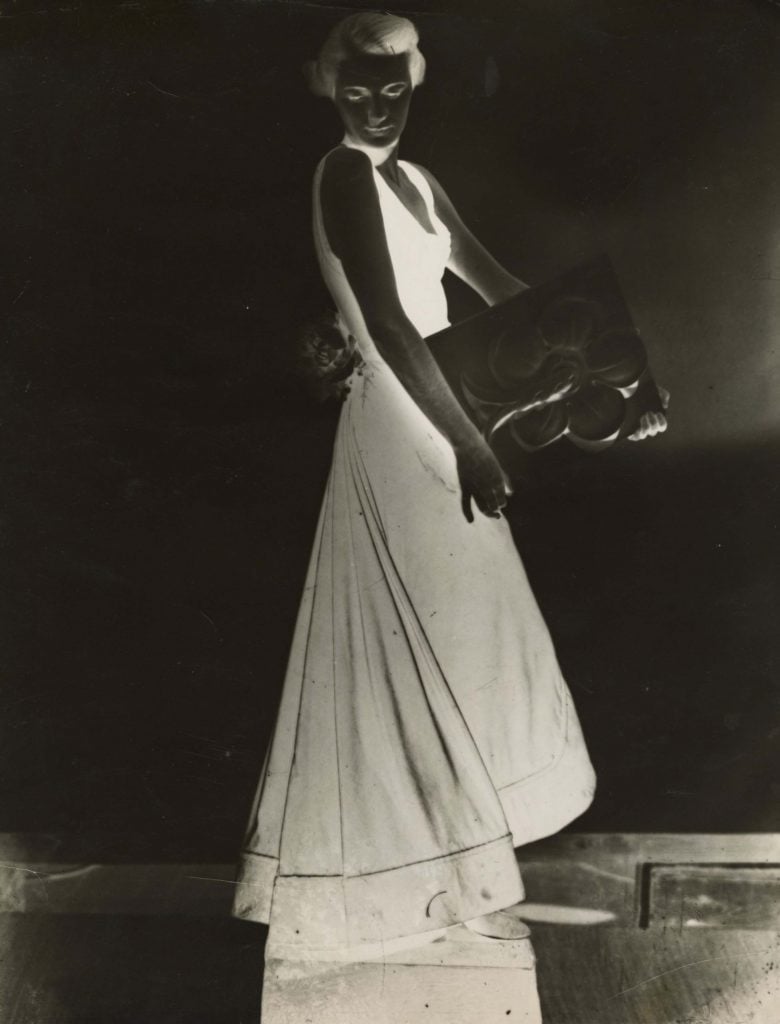 A surreal black-and-white image of a woman in an elegant gown, holding an abstract object, with a high-contrast, inverted effect.