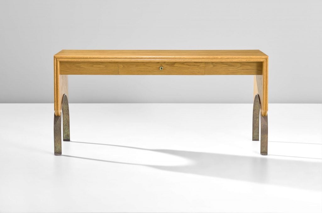 an oak table has an arched leg with metal inlay 