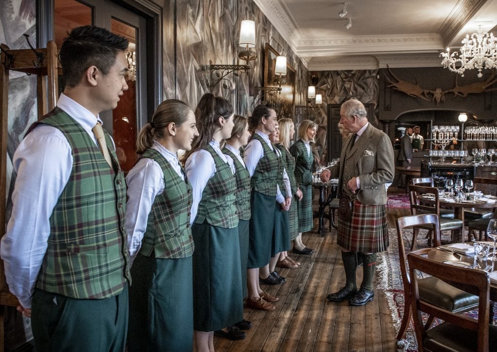 King Charles greets staff in tartan uniforms inside the Fife Arms dining room.