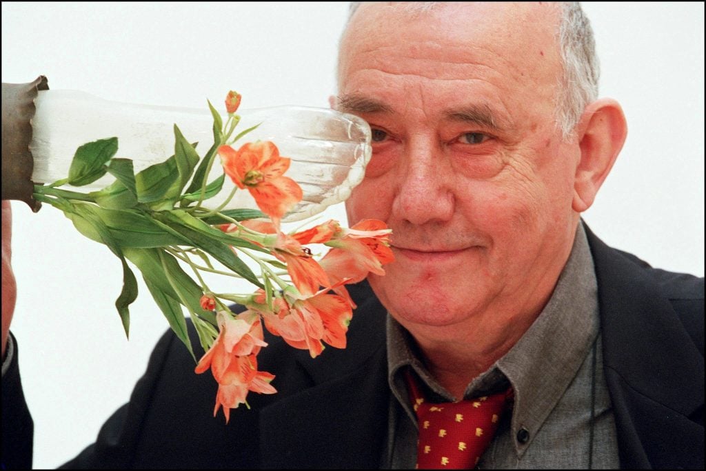 an elderly white man stands behind a sculpture of a flower