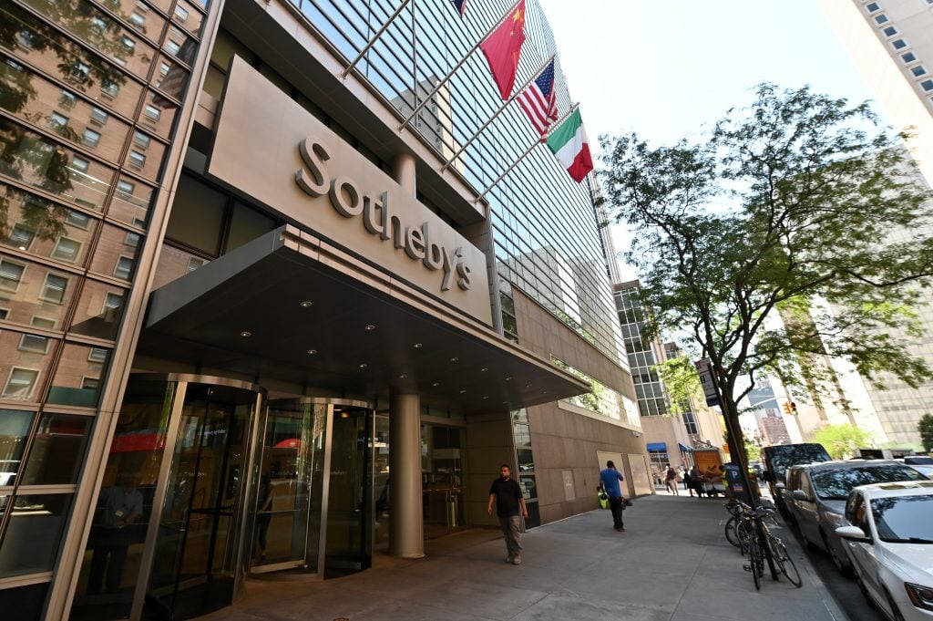 the exterior of a large office building with many flags flying outside. large letters read sotheby's above the door