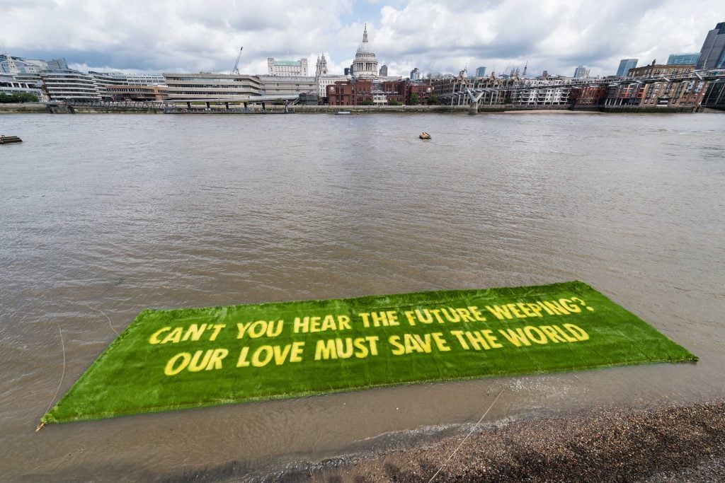 A large green floating installation on the Thames with the words, 