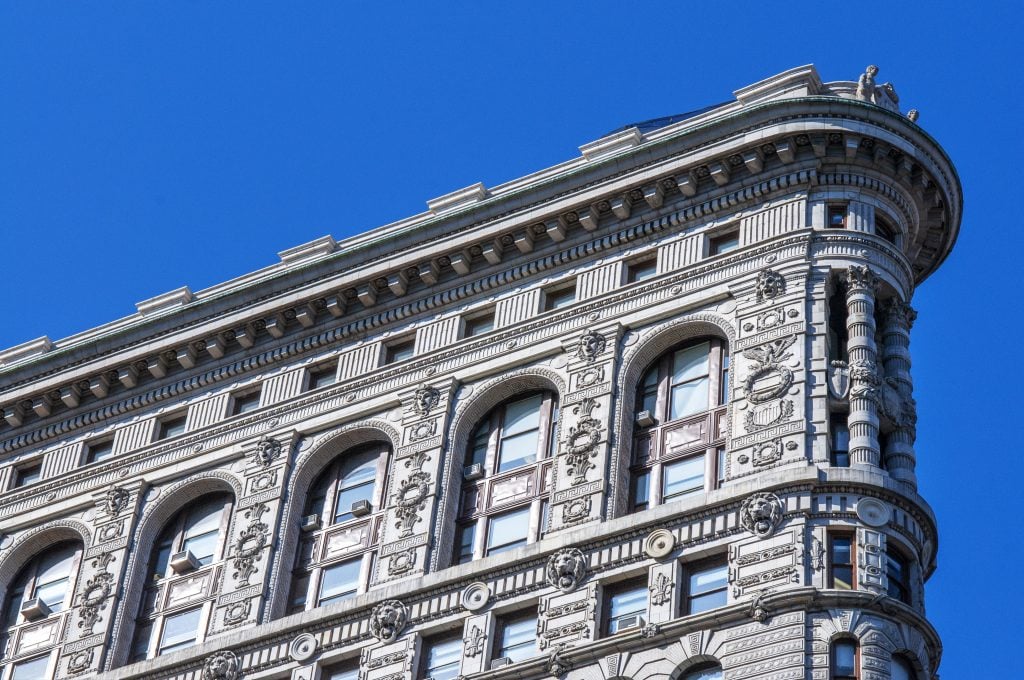 a close up photograph of the intricate beaux-arts design of the flatiron building against a blue sky