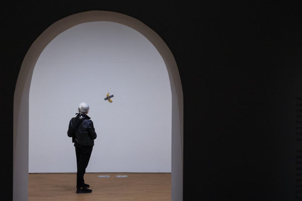 a woman standing under an arched entryway looks at a banana duct taped to the wall