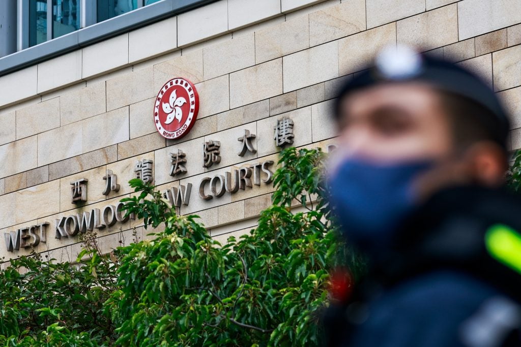 A police officer stands in the foreground outside the West Kowloon Law Courts building in Hong Kong, with its official emblem displayed prominently.