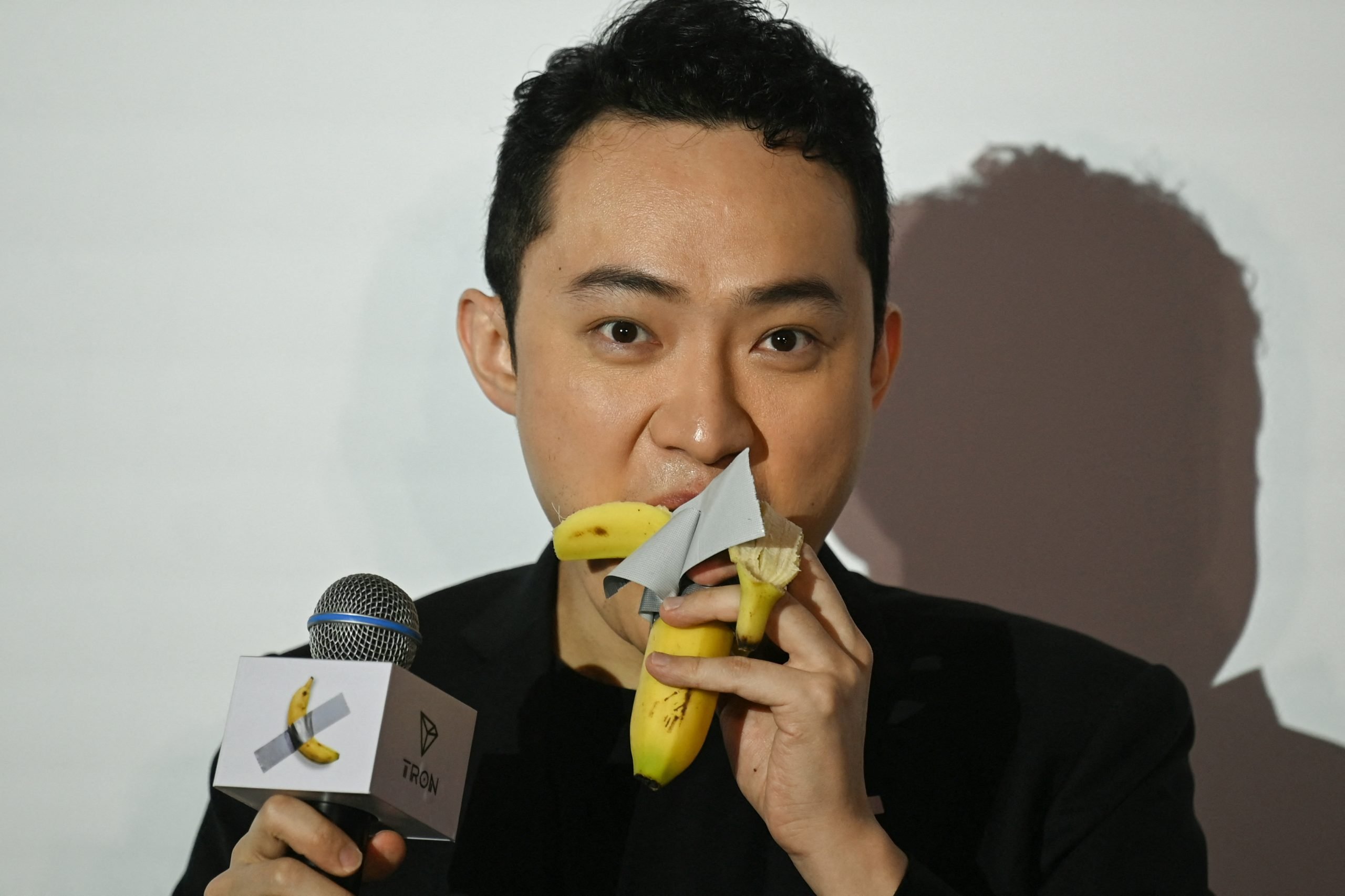 a man speaking into a microphone eats a banana while looking directly into the camera