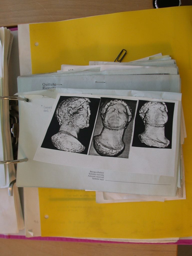 Three black and white photos of an ancient marble sculpture printed on a page attached to a pile of documents 