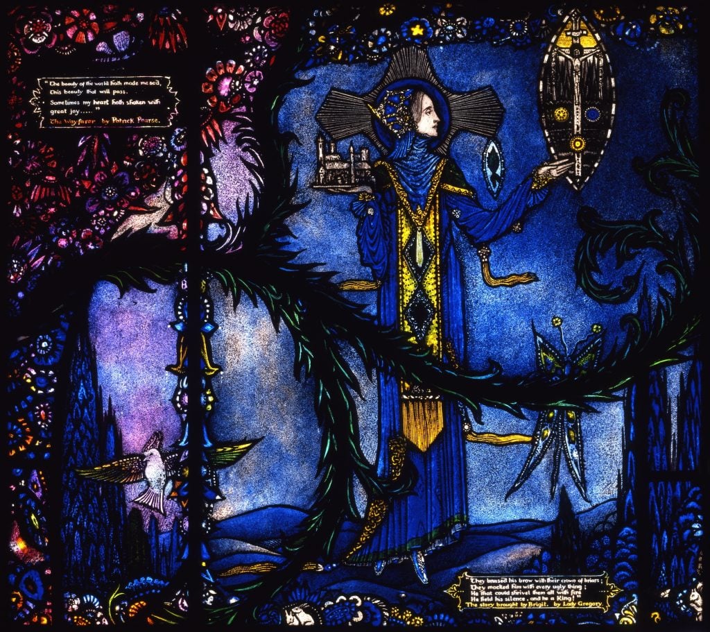 Harry Clarke, The Wayfarer by Patrick (Pádraig) Pearse and The Story Brought by Brigit by Lady Gregory from Harry Clarke Geneva Window (1926–30). A beautifully rendered stained glass window pane with a lines of poetry against an ornate purple background on the left, and a woman with a halo in a blue gown holding up an image of Jesus on the cross on the right. 