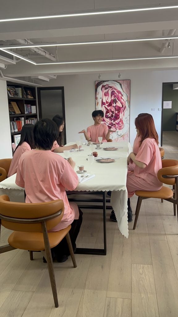 Several young people in pink T shirts sit around a table