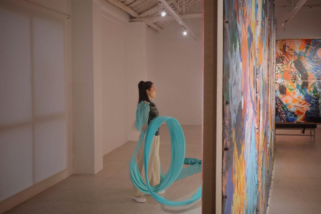 a woman in turquoise swirls around in front of paintings