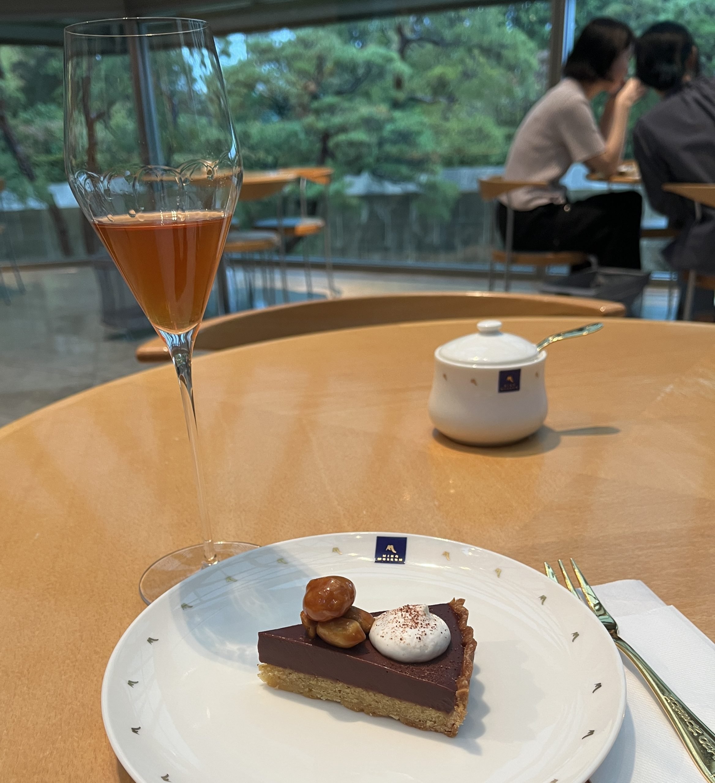 A glass of orange wine sits on a table next to a chocolate tart