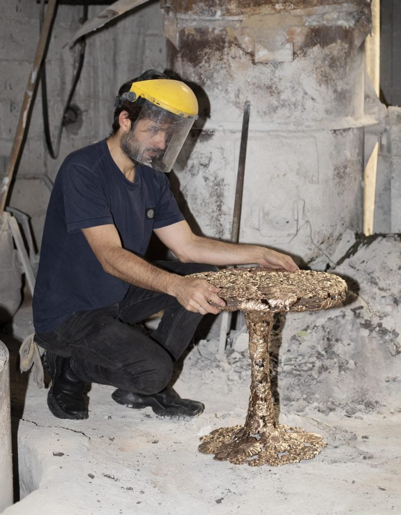 a man wearing a protective mask squats in front of a metal table in a studio 