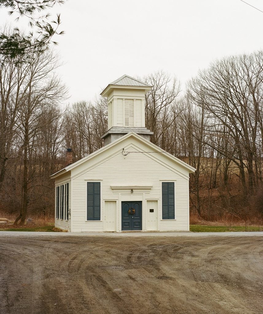 a small white clapboard church set in a wooded ground .