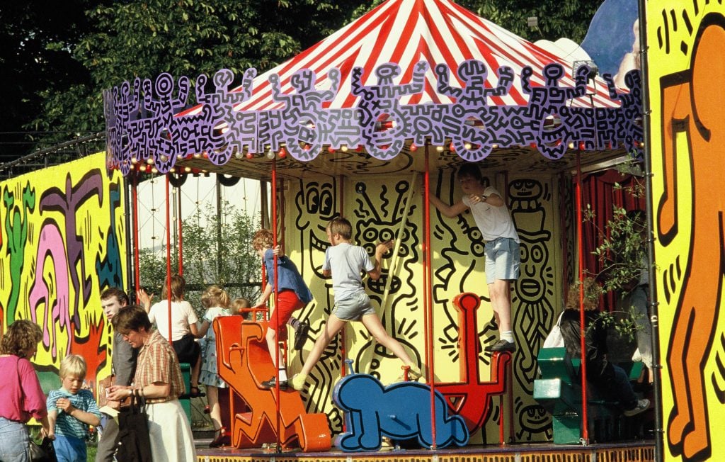 Children clamor over a carousel designed by Keith Haring, with its seats designed in his iconic cartoonish style 