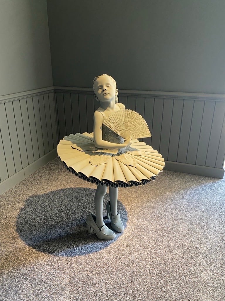 an image of a little girl in a tutu holding a fan and wearing too-big heeled shoes