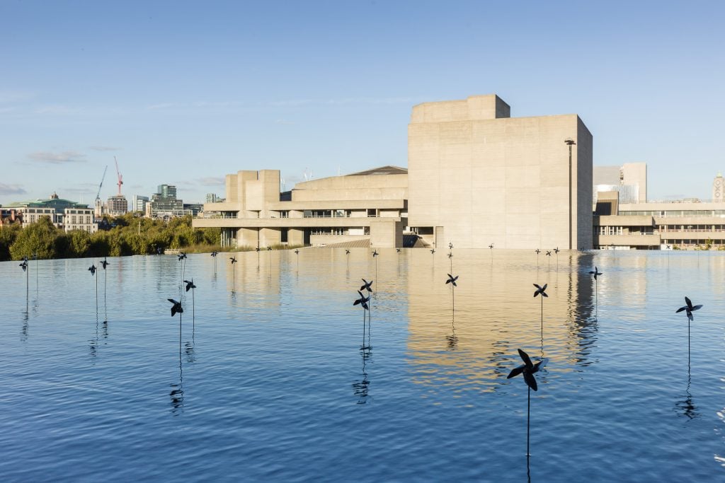 an outdoor art installation featuring a shallow expanse of water dotted with small fan sculptures