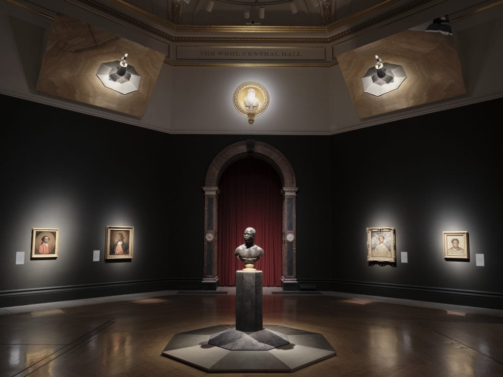 a dark exhibition hall with spotlit plinths and statues