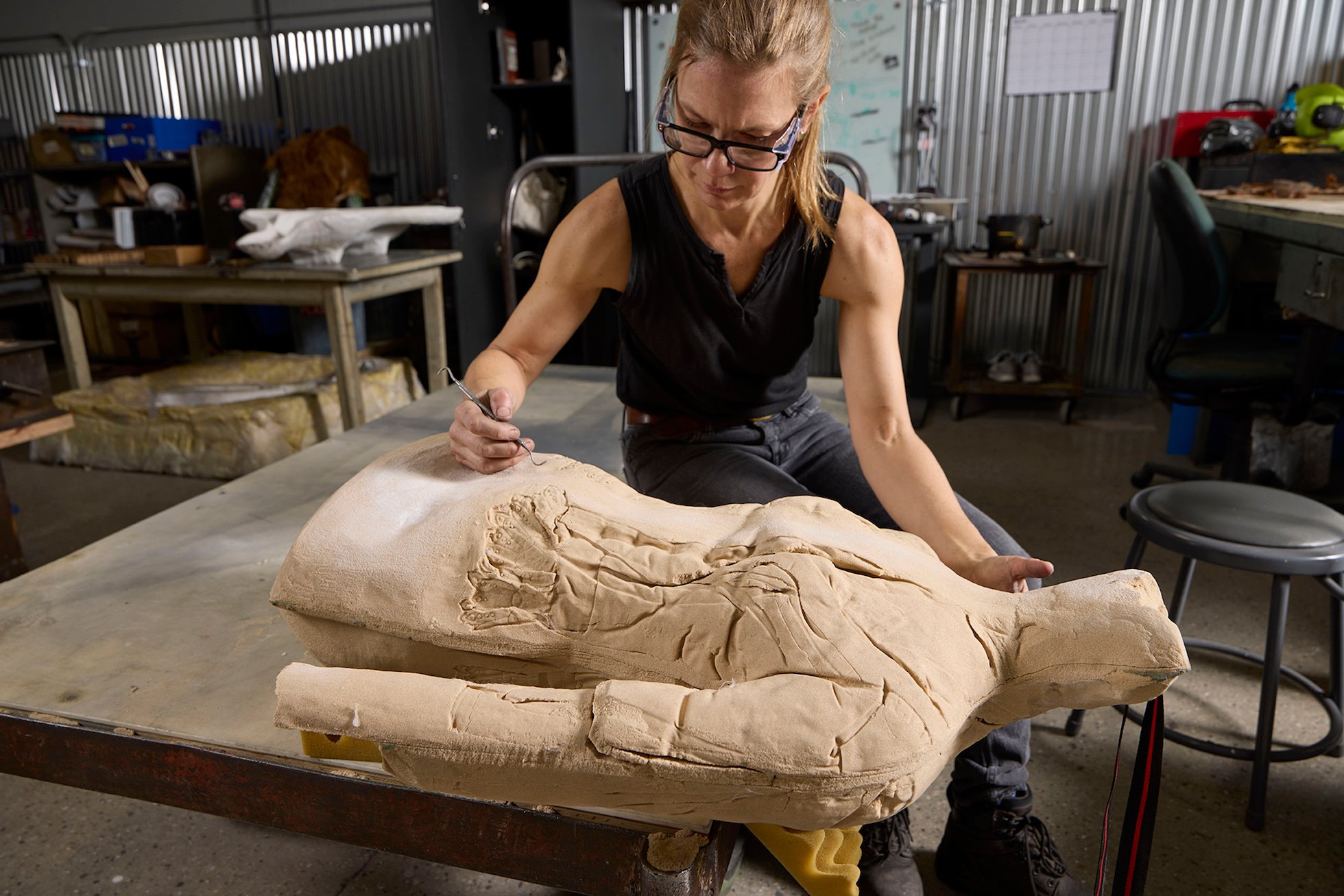 A woman in a fabrication studio works on a ceramic cast of a human body