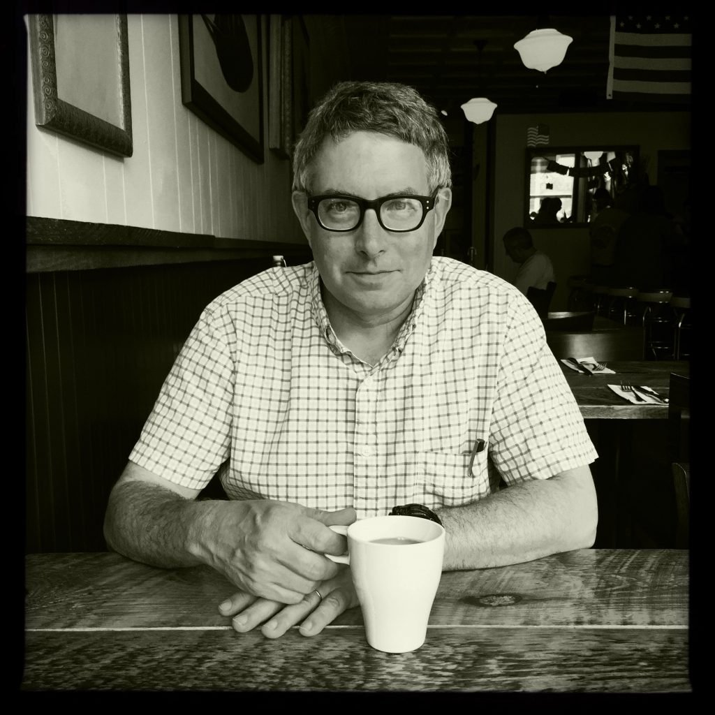 a black and white portrait of a man sitting at a diner table