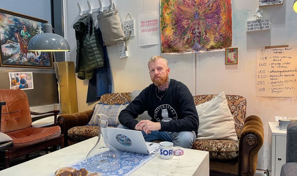 a man sits in a room full of art supplies and artworks