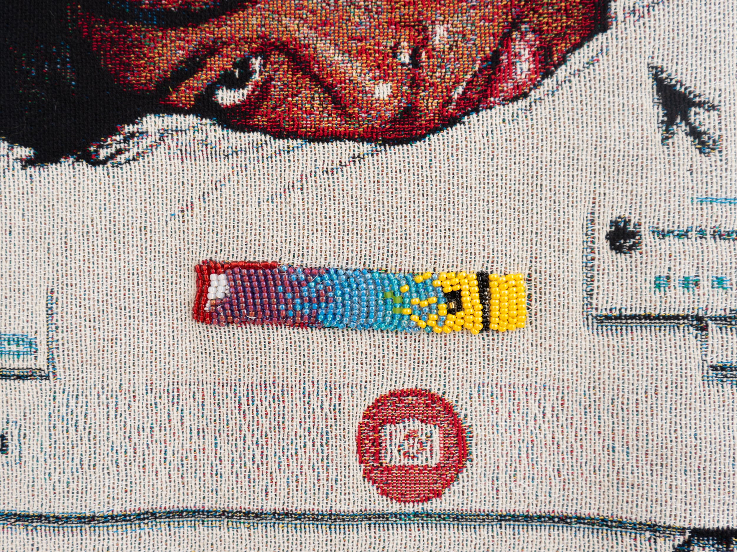 A close-up of a tapestry featuring a detailed beaded element and a partial image of a face with digital interface motifs.