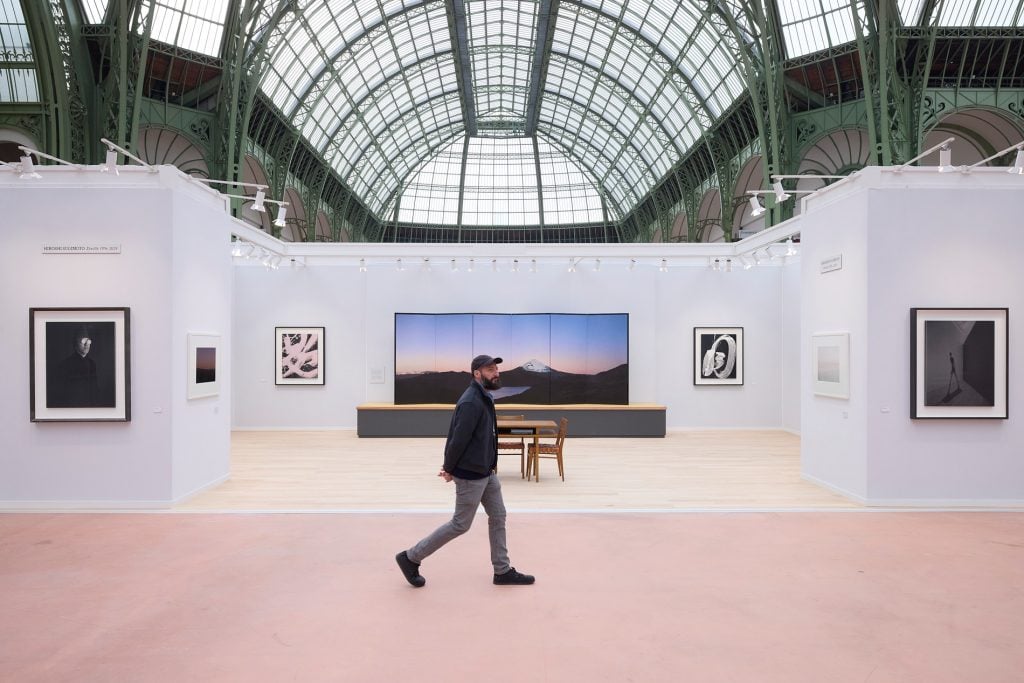 a man walks through a large exhibtion space with large arched glass ceilings