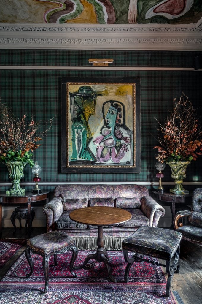 Elegant room with tartan walls, a Picasso painting, floral decor, and vintage furnishings