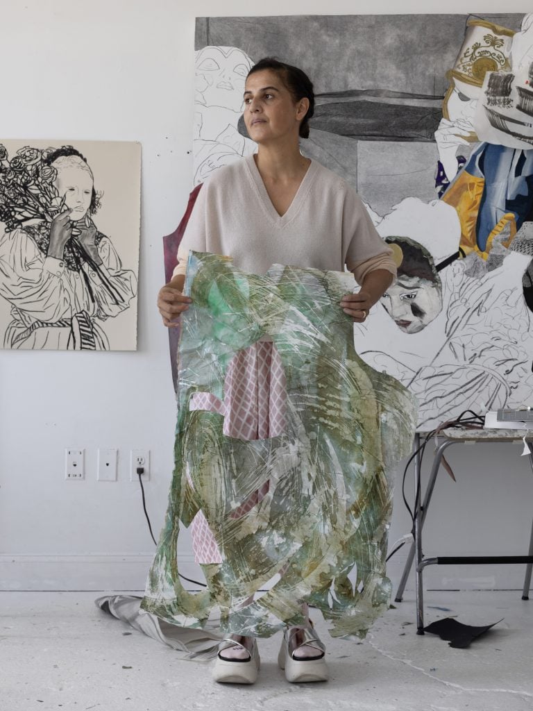 a portrait of a woman in a white studio surrounded by artwork