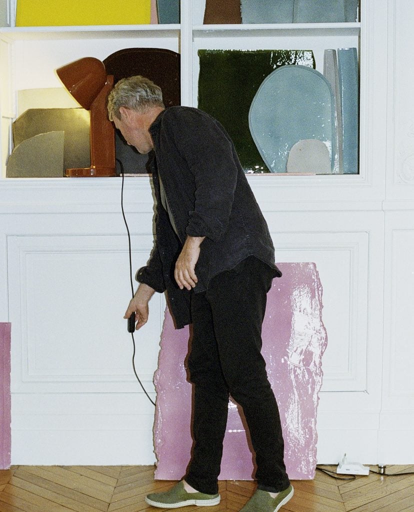 a man is in front of a wall of various art works and is turning on a modern design lamp 