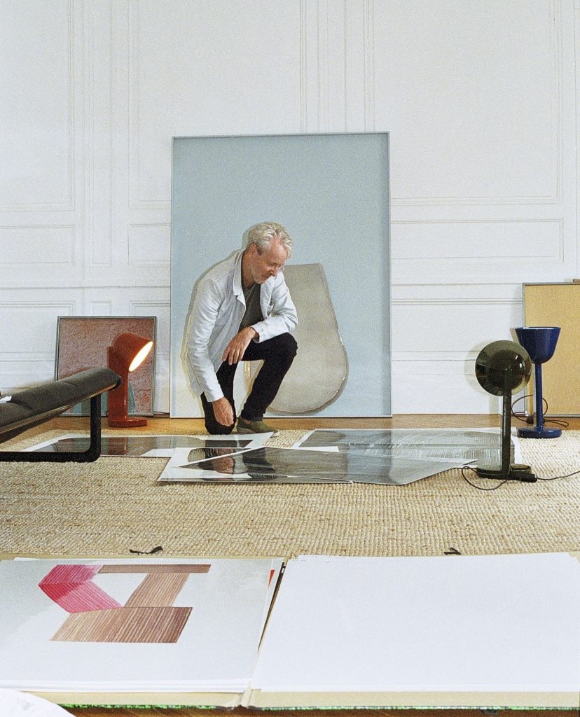 a blonde man Ronan Bouroullec is surrounded by his artwork and lamps he made and designed