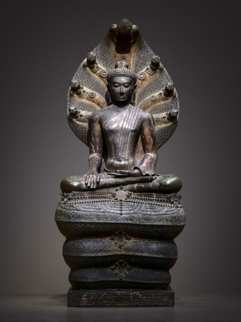 A bronze sculpture of a buddha seated under a seven-head naga's hood