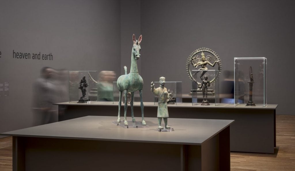 Installation view of an exhibition of bronze sculptures. In the center is an ancient piece of a horse and a man.