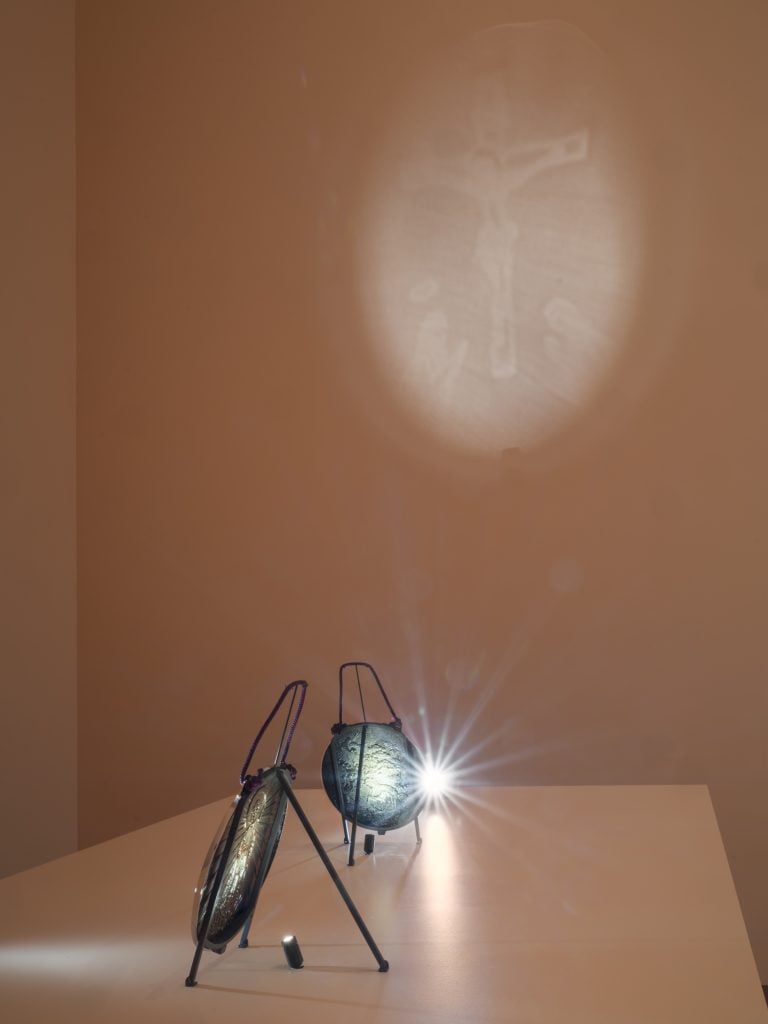 An installation of two mirrors on a table, reflecting a light and projecting an image of Jesus on crucifix.