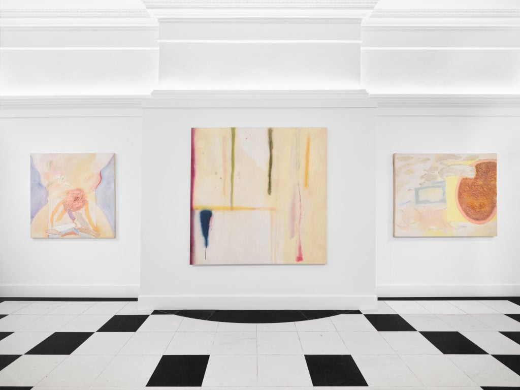 A room with a chequered floor and three abstract paintings hanging on the wall