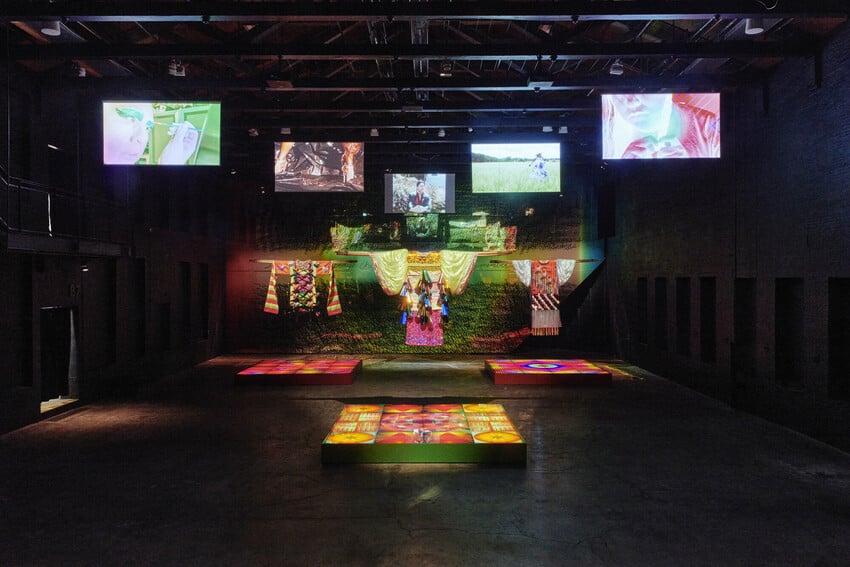 an art installation in a dark room with colourful garments hung up and LED screens