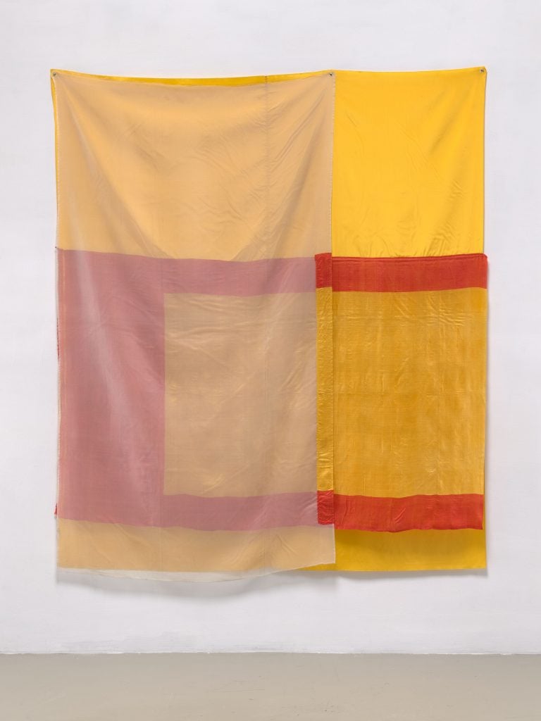 a yellow fabric with red lines across it hangs on a white wall