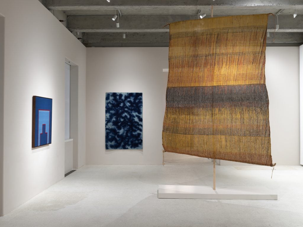 an installation view of two blue-hued tapestries and a large yellow and blue work