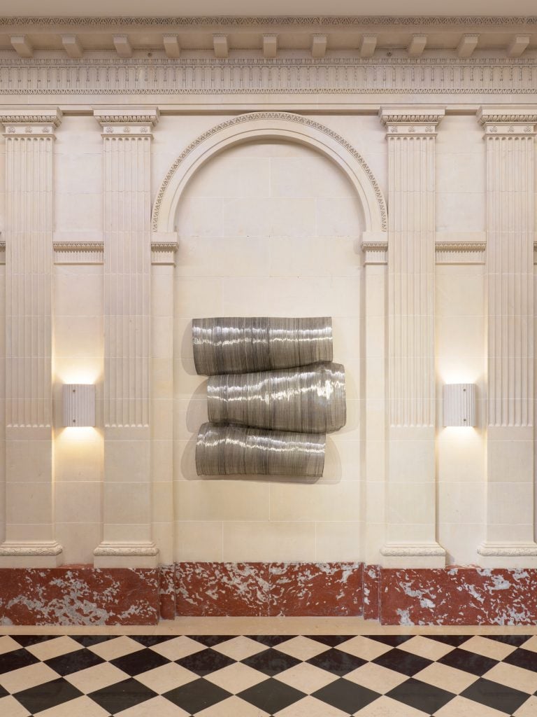 a large coiled wire sculpture hangs in an ornate hallway